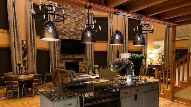Una cocina con una isla central, encimeras de granito y horno empotrado. Hay lámparas colgantes sobre la isla y una chimenea de piedra al fondo.