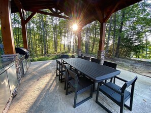 An outdoor patio with a long table and chairs, surrounded by stone walls and a wooden pergola. - A mountain experience seen from above…a view that takes your breath away! (Jamestown)
