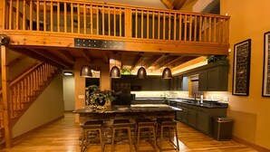 Una cocina amplia con una isla central, taburetes de madera y un entrepiso con balcón.