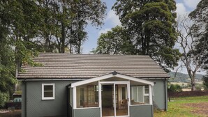 Ein eingeschossiges Haus mit Satteldach, einer überdachten Veranda und einem umzäunten Garten.