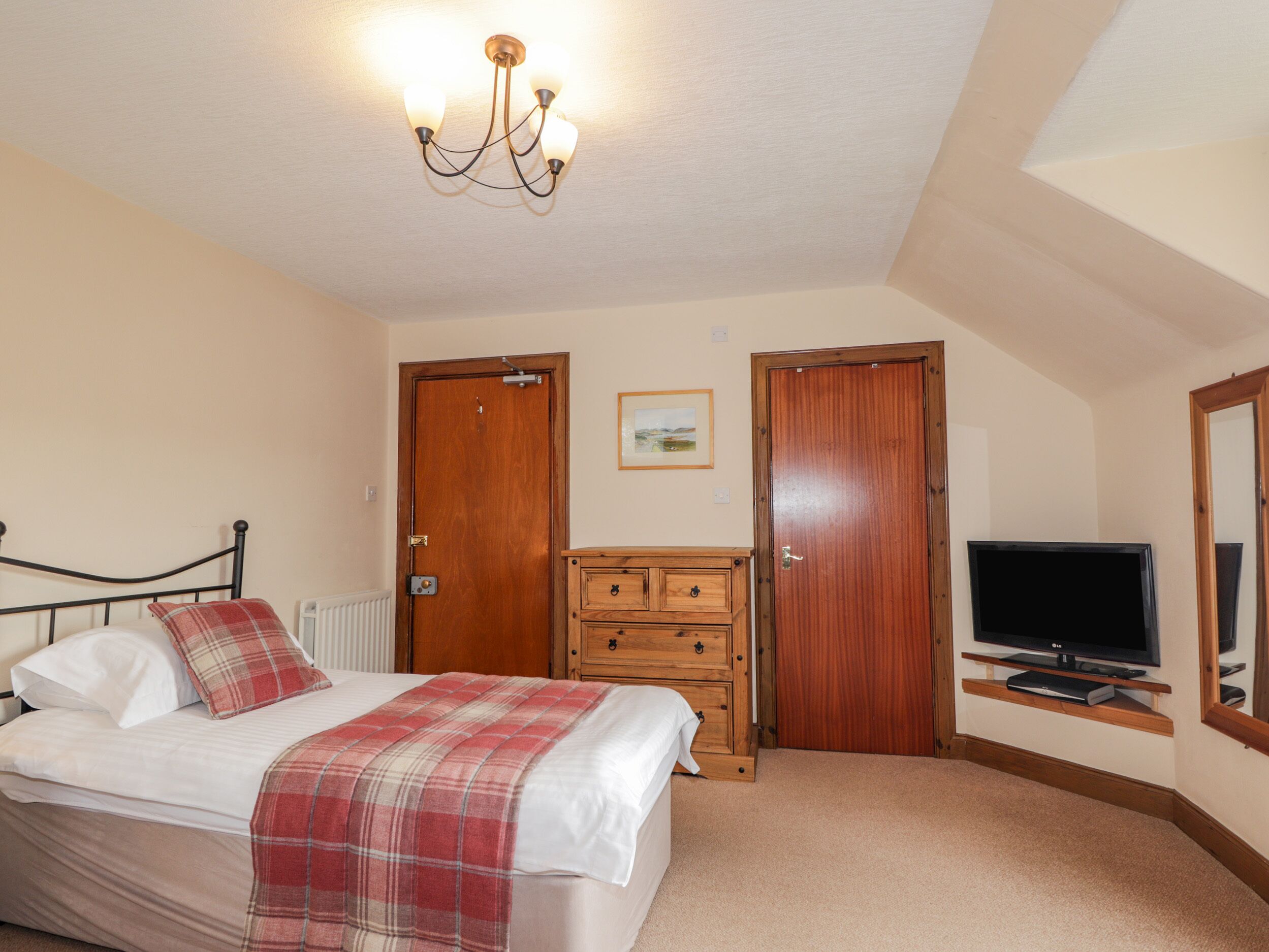 A bedroom with a bed, a wooden dresser, a television, and two doors.