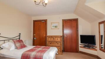 A bedroom with a bed, a wooden dresser, a television, and two doors.