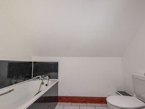A small, white bathroom with a white bathtub, a white toilet, and a wooden floor. - Balloan House (Muir of Ord)