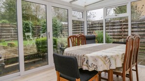 Une véranda équipée d’une table et de chaises, de grandes portes vitrées et offrant une vue sur un jardin.
