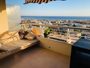Enjoy the stunning city and sea views from this balcony's comfortable seating area.