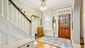 Una escalera con balaustres blancos, suelo de madera, un banco blanco, un radiador, otro radiador blanco, una puerta de madera y una alfombra azul estampada.