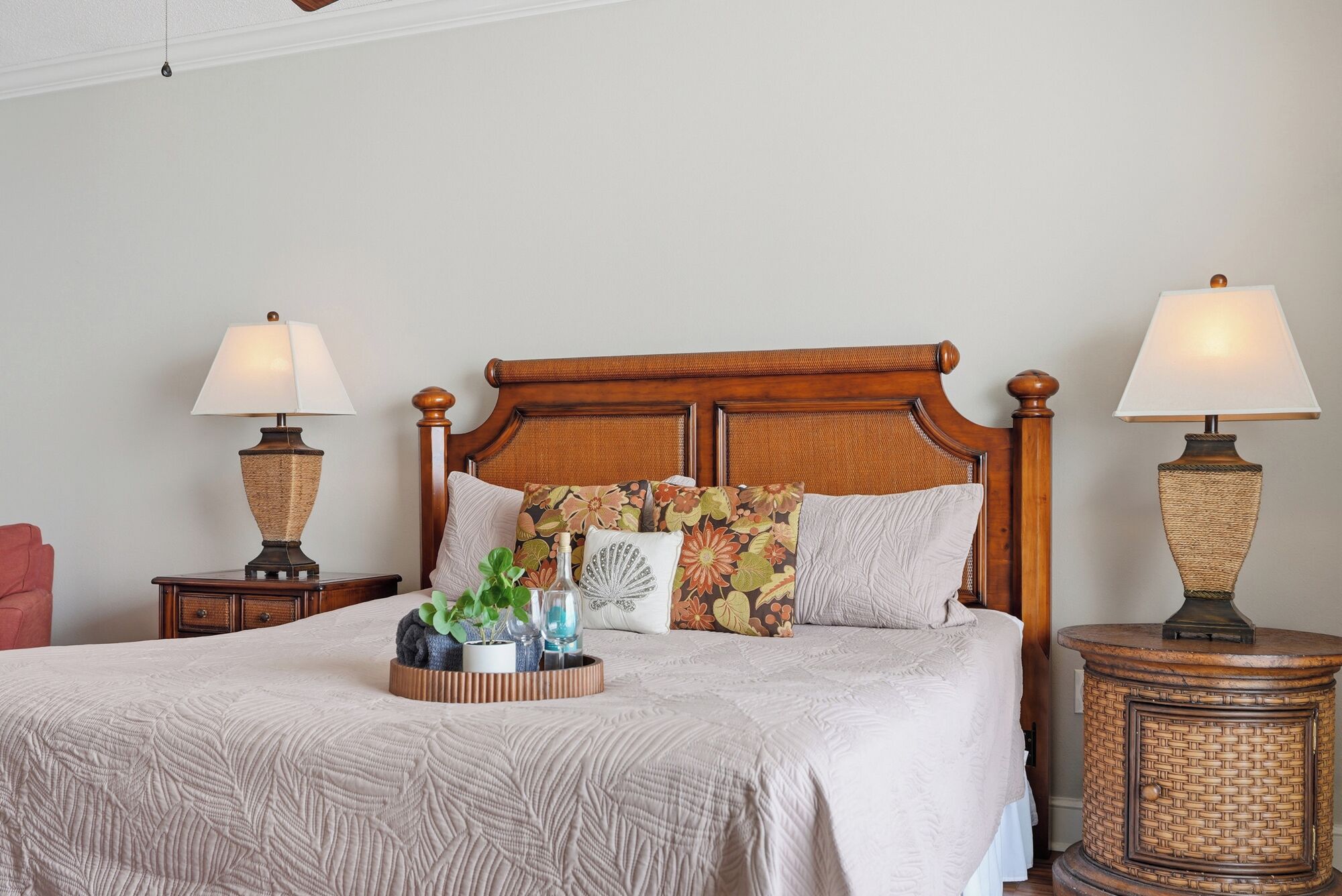 A neatly made bed with a wooden headboard, two bedside tables with lamps, and a bedside plant.