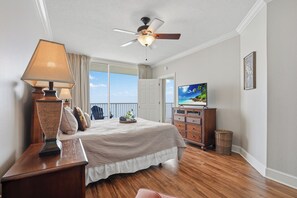 Quarto com cama, ventoinha no teto, televisão, penteadeira e janela com vista.