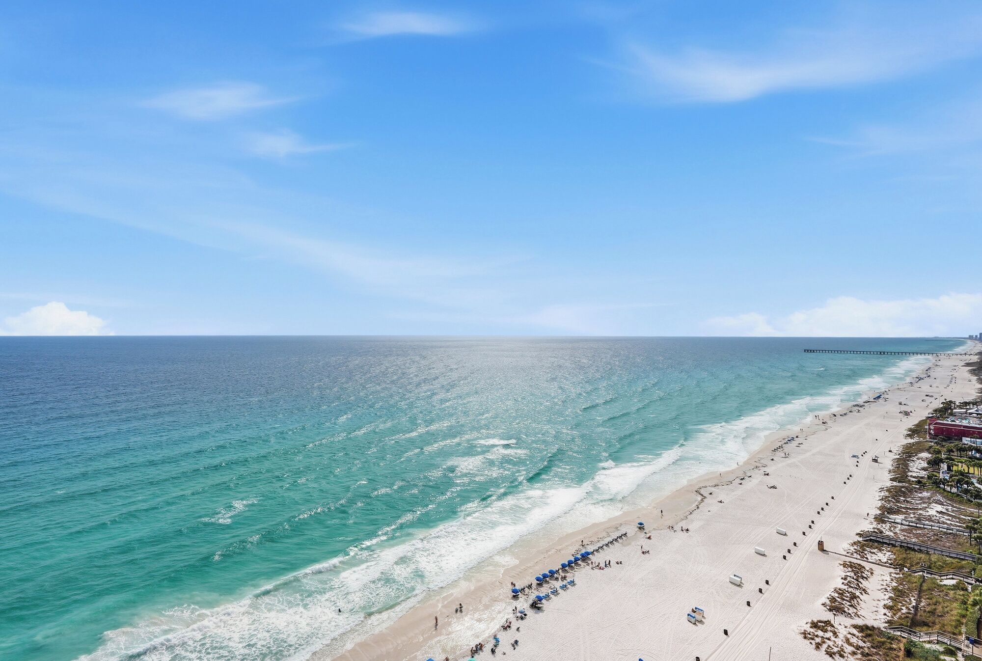 A beach with a pier, clear skies, and calm waters.