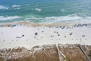 Vista aérea de uma praia com areia, ondas e algumas pessoas.