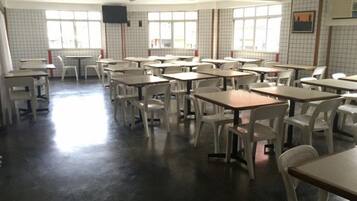 Un aula con mesas y sillas dispuestas en filas, ventanas amplias y una pantalla para proyector.