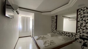 Un dormitorio con cama, ventana con cortinas, televisor montado en la pared y un espejo de diseño geométrico.