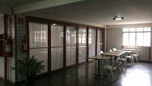 Una habitación con pared de azulejos, una planta en maceta, un extintor y una fila de mesas y sillas.