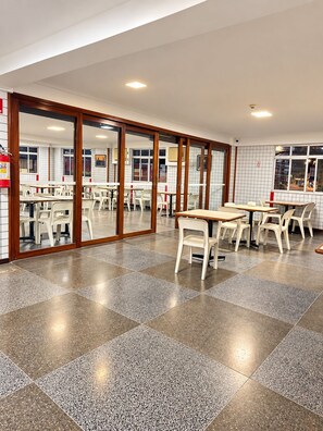 A spacious indoor area with multiple tables and chairs, large windows, and a tiled floor. - Hotel Novo Plano (Salvador)