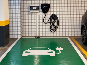 A parking space with a green floor marked for electric vehicles, a charging station, and a car parked to the right. - Hotel Novo Plano (Salvador)