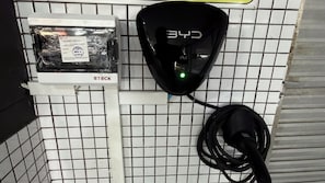 A wall-mounted device with a cable connected to it, a box labeled 'STECK' with a certification sticker, and a grid-patterned tiled wall. - Hotel Novo Plano (Salvador)