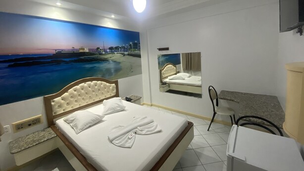 Una habitación de hotel con cama, ventilador de techo, un gran mural en la pared que muestra una playa, espejo y televisor montado.