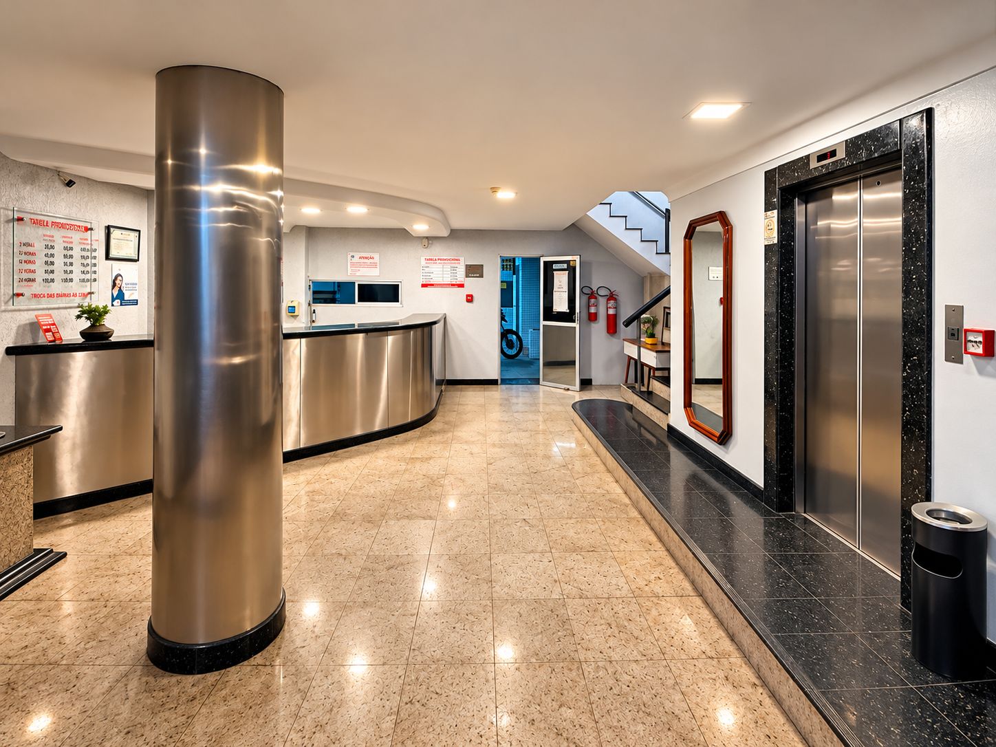 A hotel reception area with a reception desk, a large pillar, an elevator, and a staircase.