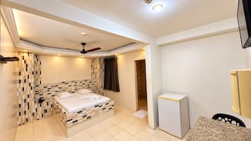 Ein Hotelzimmer mit einem Bett, einem Deckenventilator, einem kleinen Kühlschrank und einem Badezimmer mit Dusche.