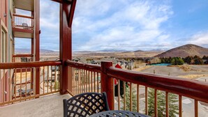 A balcony with a view of a mountainous landscape, a wooden railing, and a table with chairs.