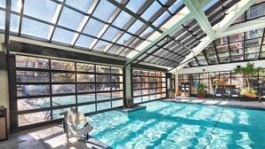 An indoor swimming pool with a glass ceiling, clear pool water, and surrounding lounge area.