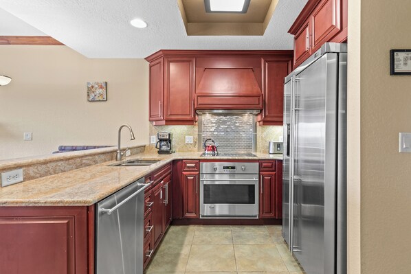 Una cocina con electrodomésticos de acero inoxidable, armarios rojos y salpicadero de azulejos.