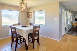 Comedor con mesa dispuesta para cuatro, ventanas amplias y cocina visible al fondo.