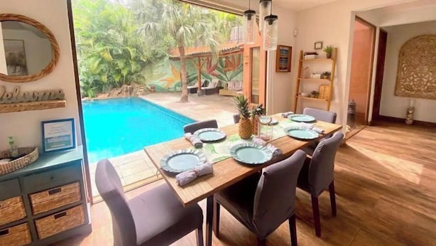 Espaço de refeições com vista para uma piscina e plantas tropicais.