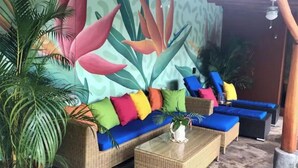 Um sofá de vime com almofadas coloridas, uma mesa de centro de vidro e uma planta grande.