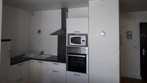 Uma cozinha compacta com armários brancos, bancada preta, micro-ondas, forno e uma luminária pendente azul.