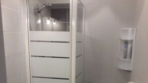Casa de banho com chuveiro em cabine de vidro, sanita e lavatório.
