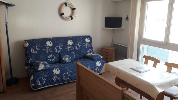 Quarto com sofá azul, mesa de madeira e televisão sobre um suporte.