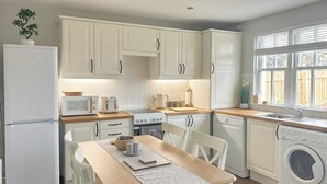 A kitchen with white cabinets, a wooden table, a refrigerator, a microwave, a stove, a sink, and a washing machine. - 2 bedroom accommodation in Colinsburgh, near Elie and Anstruther (Colinsburgh, near Elie and Anstruther)
