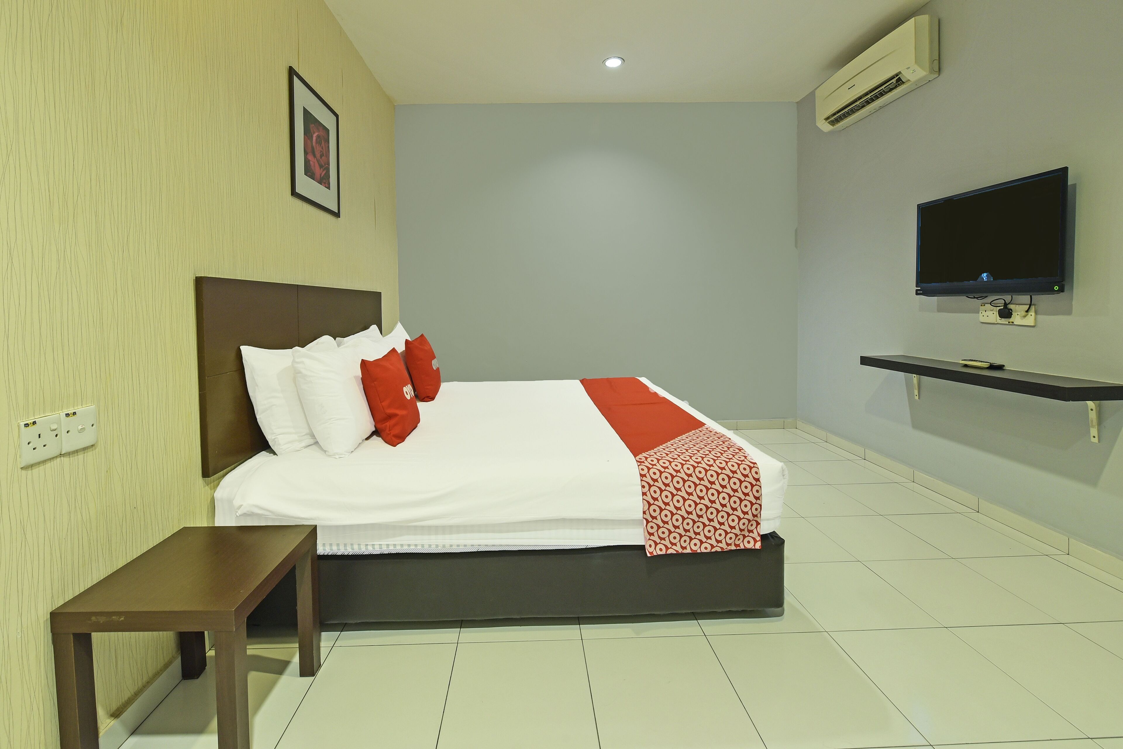 Een hotelkamer met een bed, een nachtkastje, een aan de muur bevestigde televisie en een airconditioning.