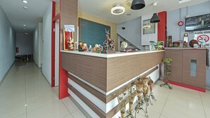 A modern reception area with a wooden reception desk, a television mounted on the wall, and various decorative items. - Hotel O M Three Hotel (Sitiawan)