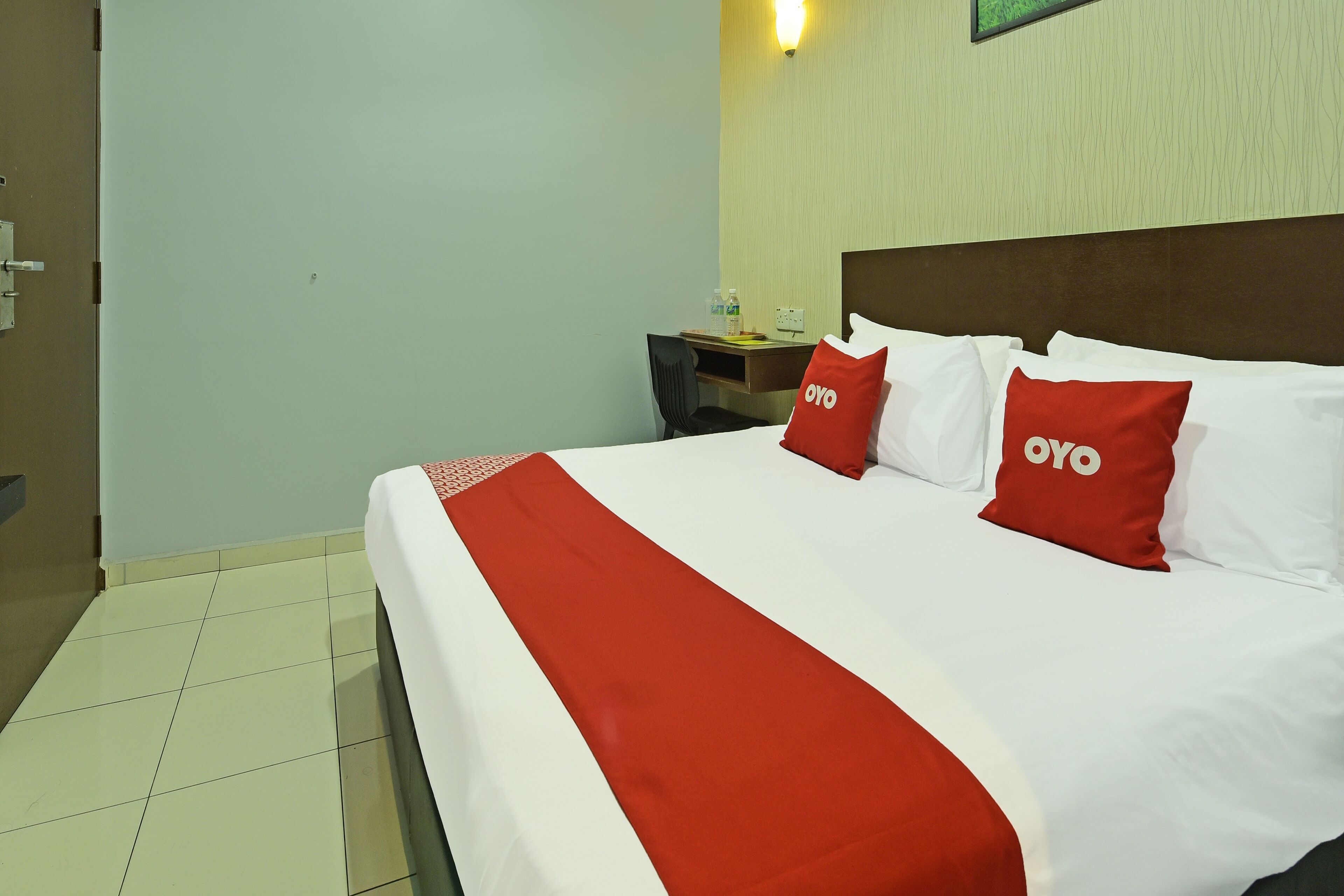 A hotel room with a neatly made bed, a nightstand with a lamp, and a chair.
