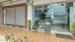 A storefront with a closed shutter, a glass door, and a sign indicating it's open. There are potted plants and chairs outside. - Hotel O M Three Hotel (Sitiawan)