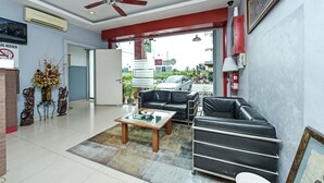 A modern living room with a ceiling fan, a glass coffee table, a black leather sofa, and a red-framed painting. - Hotel O M Three Hotel (Sitiawan)