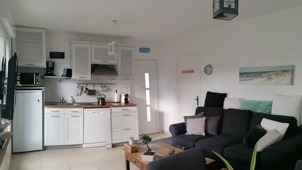 Een moderne keuken met witte kastjes, een koffiezetapparaat en een magnetron. Er is een eethoek met een houten tafel en stoelen, en een zwarte bank met kussens.