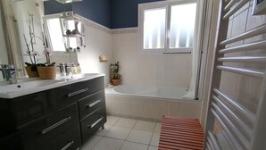 Een moderne badkamer met een donkerblauwe accentmuur, een witte wastafel met spiegel, een badkuip en een houten bankje.