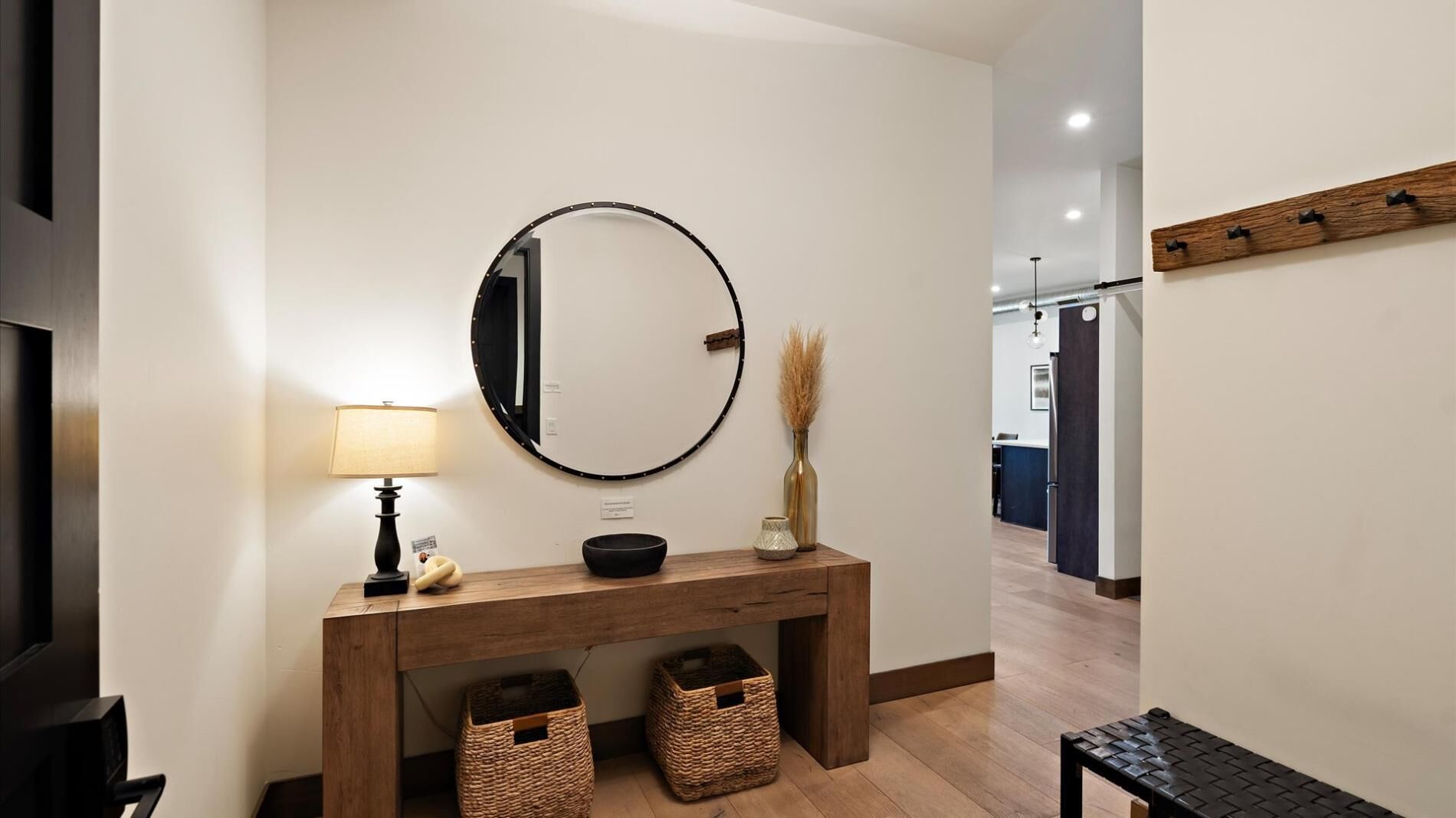 A modern hallway with a wooden console table, a round mirror, a lamp, and two baskets.