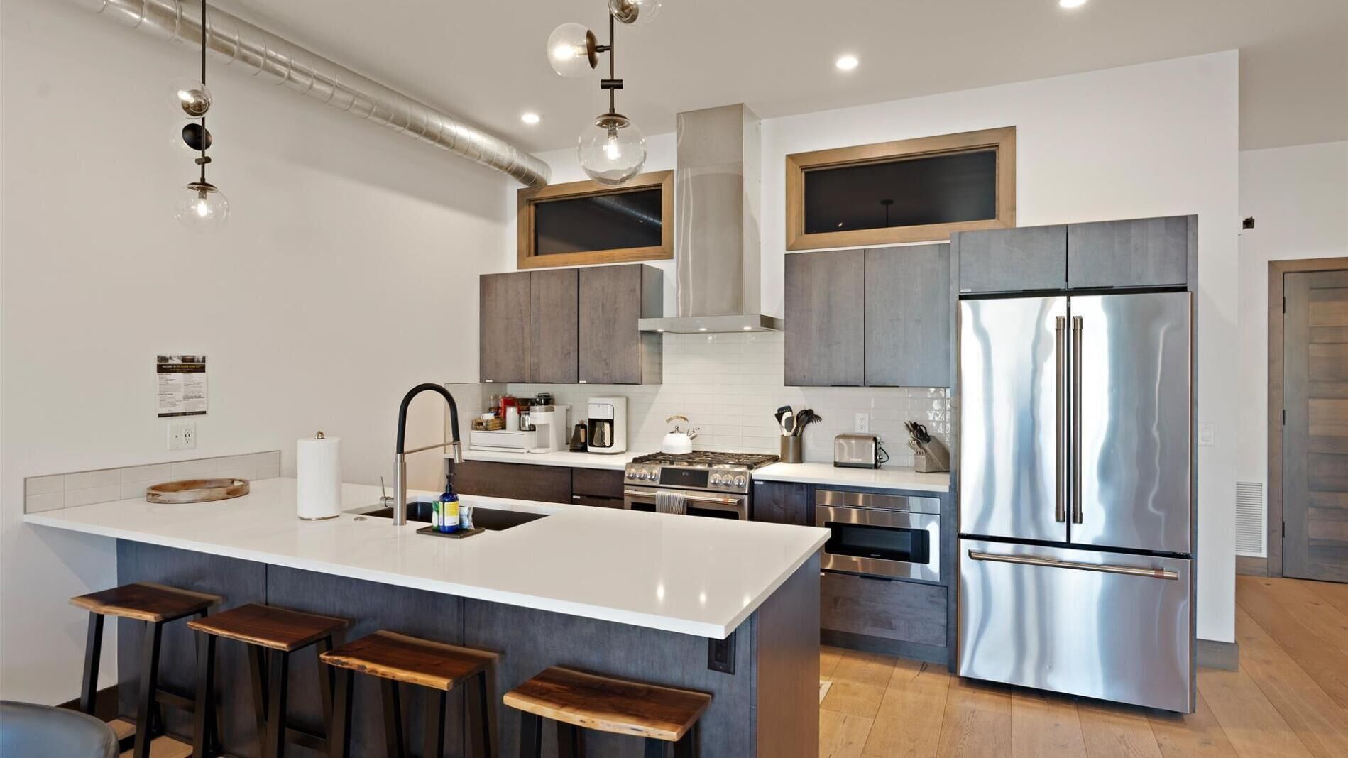 A modern kitchen with a central island, stainless steel appliances, and bar stools.