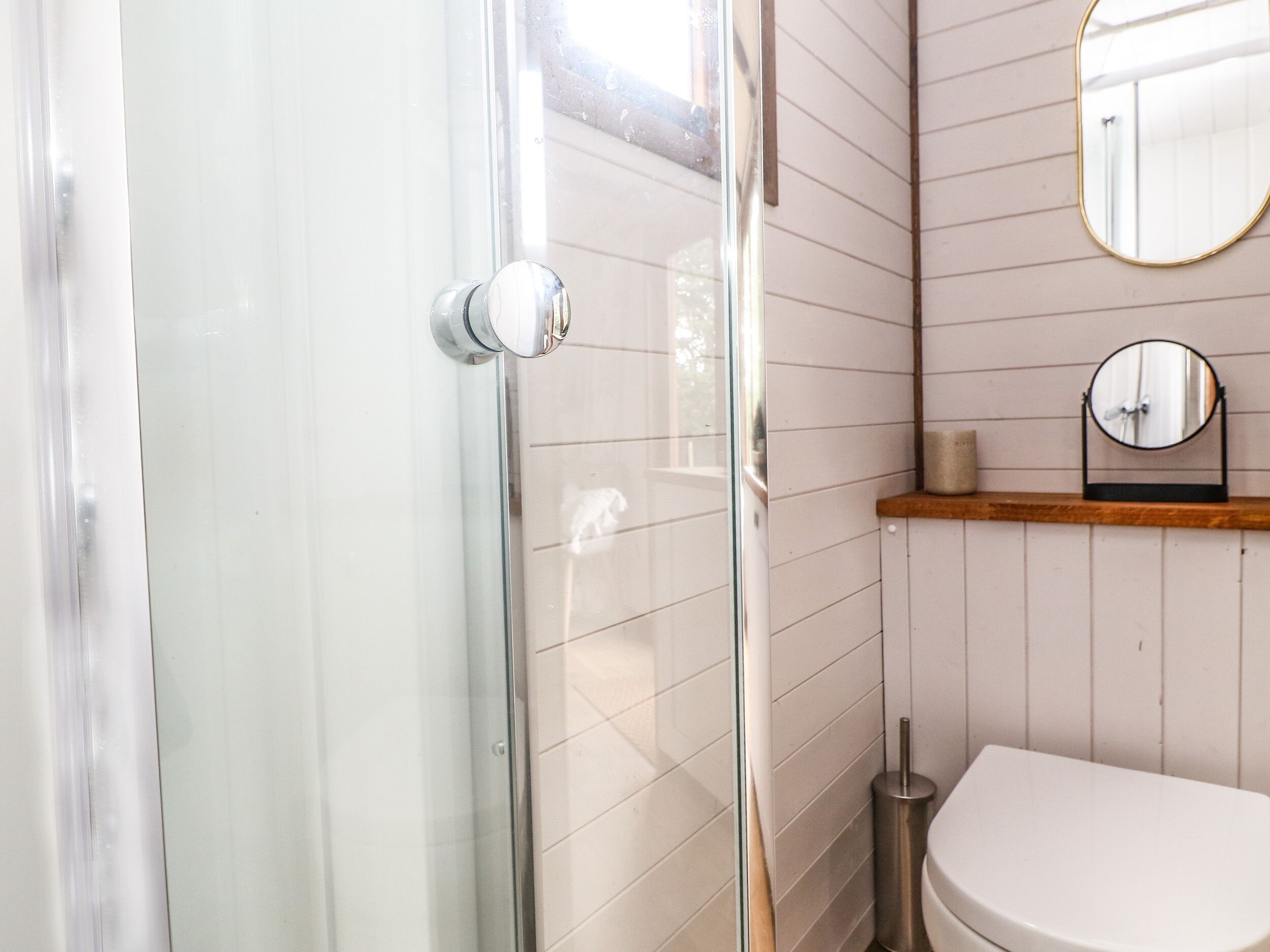 A bathroom with a glass shower door, a toilet, a sink, and a mirror on the wall.