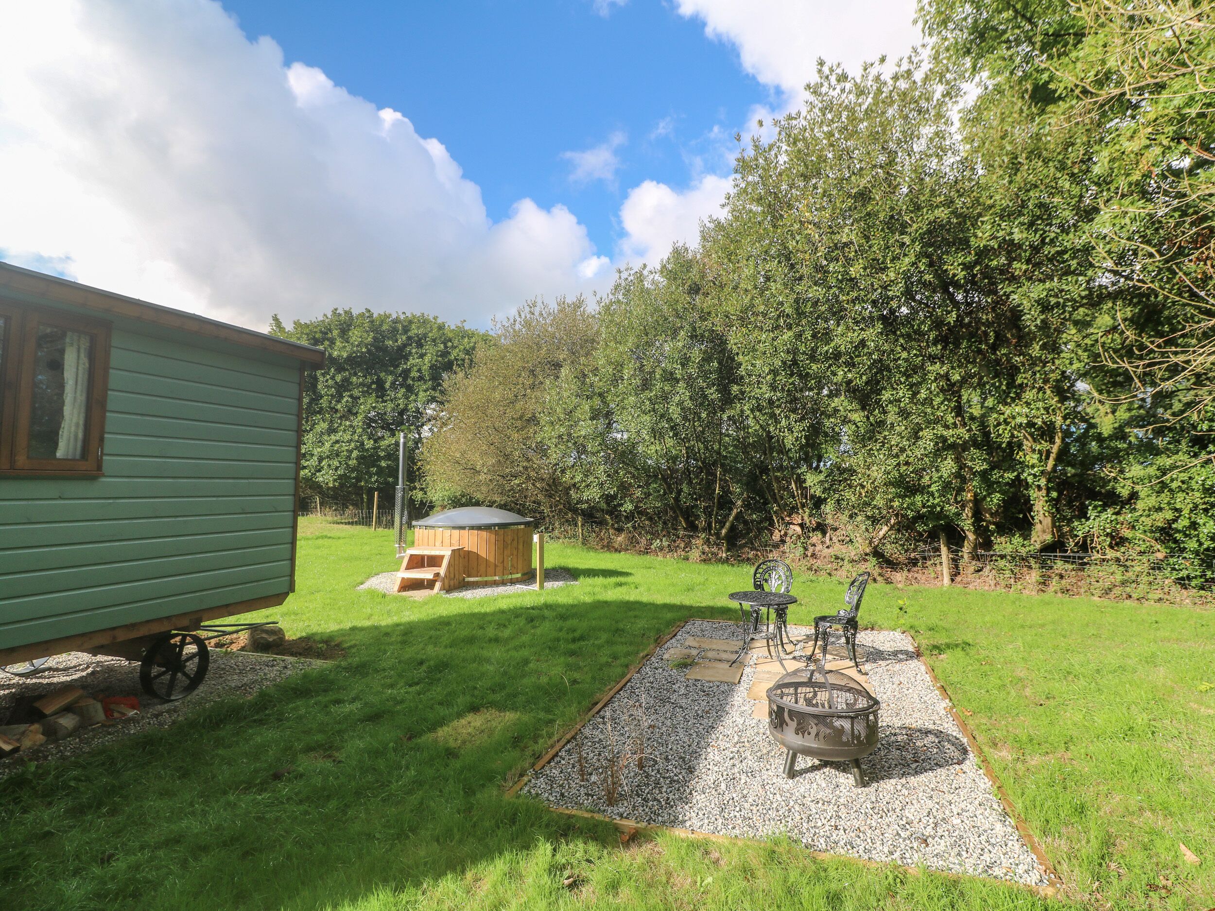 A green mobile home with a small deck and a fire pit area with outdoor furniture.