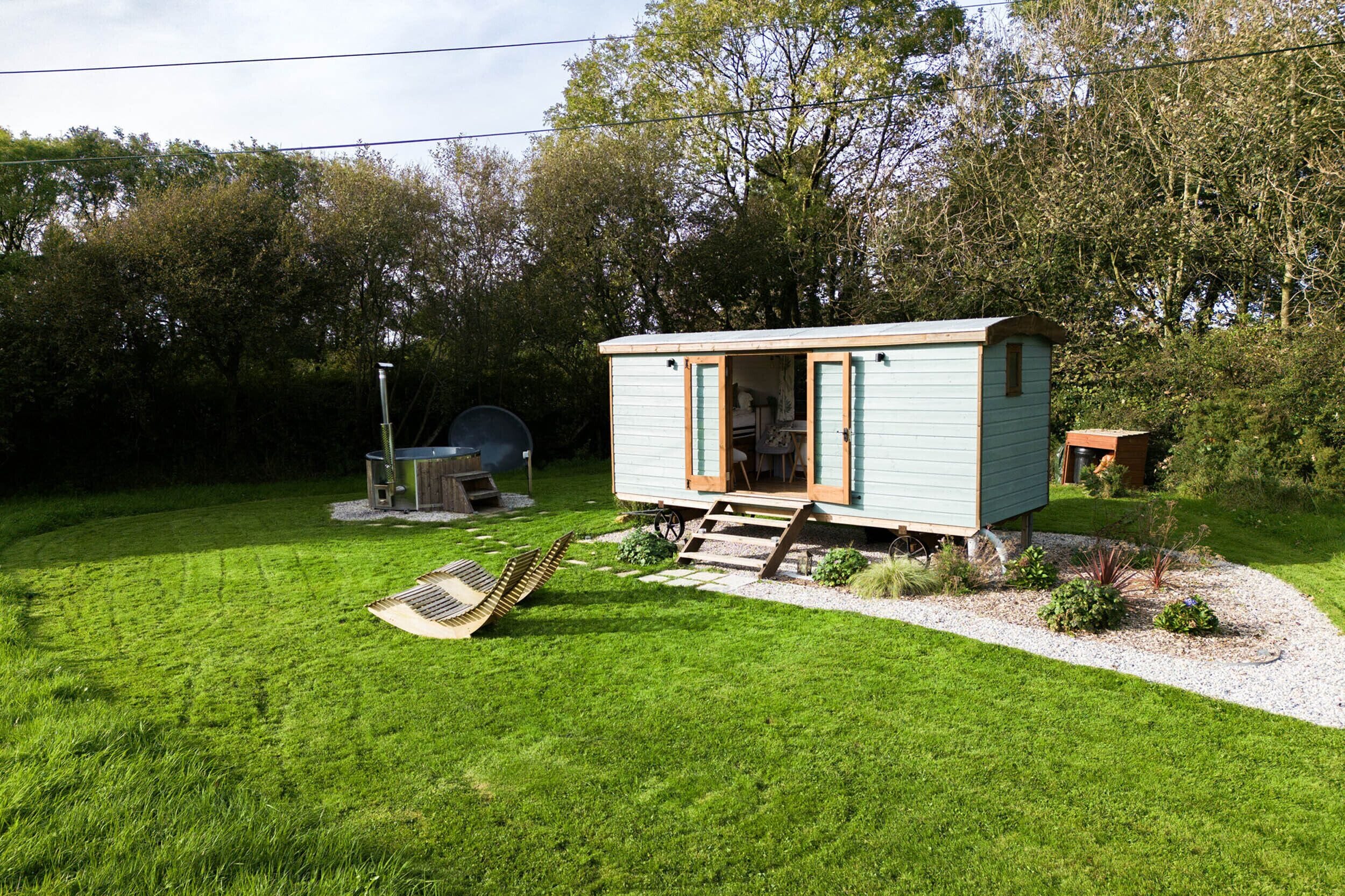 A small, light blue cabin with a wooden deck and a bicycle in the yard.