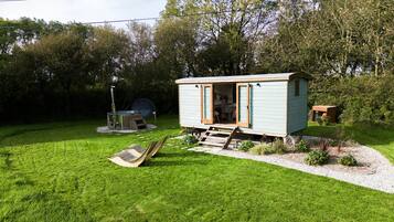 A small, light blue cabin with a wooden deck and a bicycle in the yard.