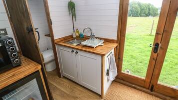 A compact kitchen with a sink, wooden countertop, and a view of a grassy yard through a glass door.