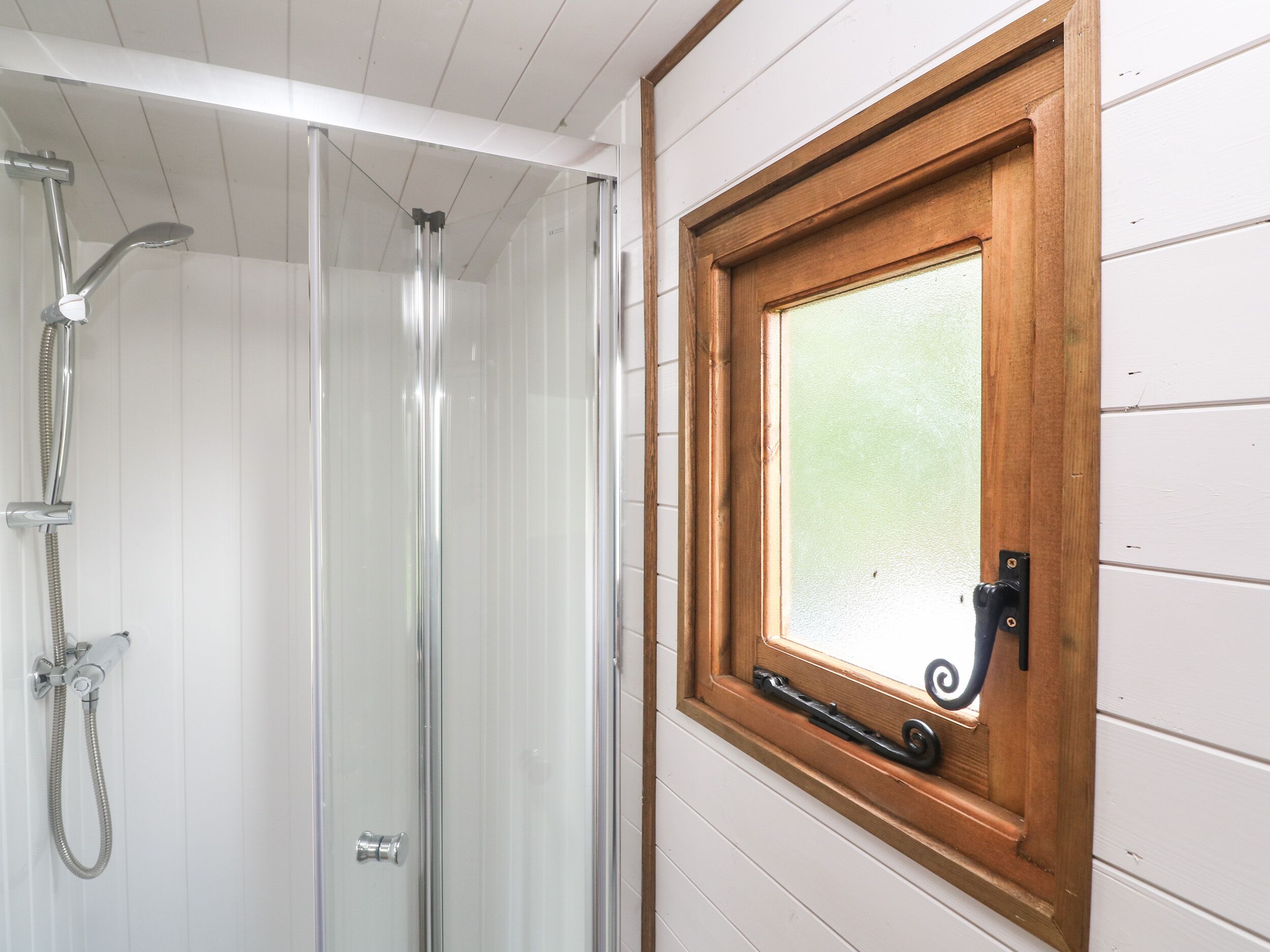 Une douche dotée d’une porte en verre et d’une fenêtre en bois avec un vitrage dépoli.