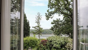 A stone patio with potted plants and a view of a lake and trees. - Ynys Castell (Menai Bridge)