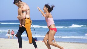 A beach scene with a man carrying a child and a woman running.